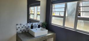 a bathroom with a white sink and two windows at Volgenoeg Self Catering Cottage in Oudtshoorn