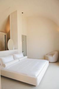 a white bedroom with a bed and a chair at VOUNO Santorini Private Villas in Pyrgos