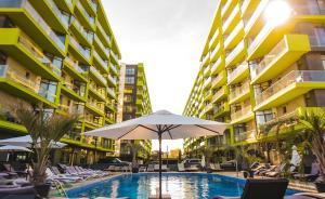 a swimming pool with an umbrella and chairs and buildings at Alezzi Luxury Double Studio - Beach Pool & Spa Resort in Mamaia Sat/Năvodari