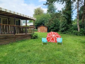two chairs and a red and white umbrella in a yard at Mobil home Vegas in Blangy-le-Château +1 photo