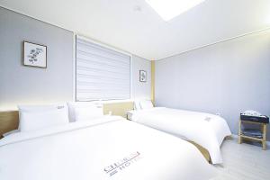 a white bedroom with two beds and a window at 통영호텔조선 in T'ongyŏng