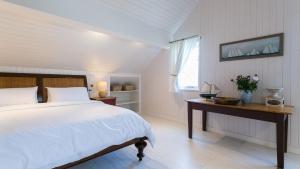 a white bedroom with a bed and a table with flowers at Brendon in Nefyn