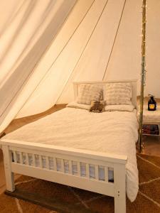 a white bed in a tent with a bag on it at Damson Keep Wild glamping pop up in Bere Alston