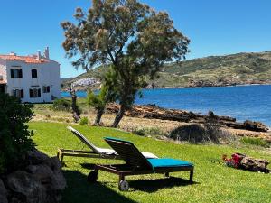 zwei Liegestühle und ein Tisch auf der Wiese am Wasser in der Unterkunft Miravent Terraza y Jardin Frente al mar Menorca in Fornells