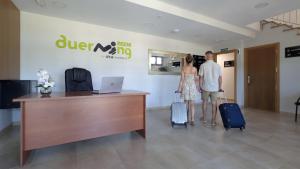 a man and woman standing in an office with luggage at Duerming La Rana Sanxenxo in Sanxenxo