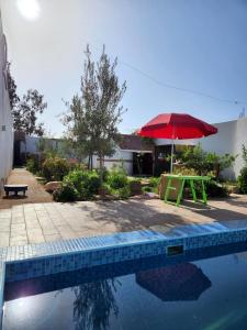 a pool with a table and a red umbrella at Séjour Traditionelle in Oulad Teïma