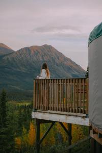 a woman sitting on a deck looking at the mountains at CabinsOver Crag Lake Glamping Bear in Carcross