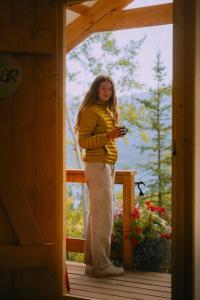 a woman standing on a porch looking at her cell phone at CabinsOver Crag Lake Glamping Bear in Carcross