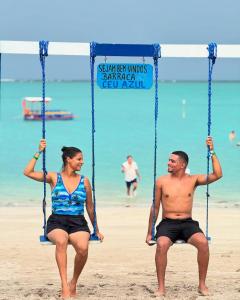 a man and a woman sitting on a swing on the beach at Pousada Vila Mar Japaratinga in Japaratinga