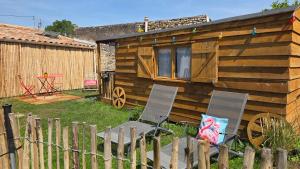 a wooden cabin with two chairs and a fence at Un aparté bohême "La Roubane" in Puyravault