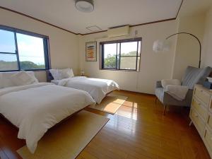 a bedroom with two beds and a chair and windows at Villa Nami in Kashima