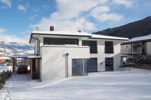 a white house in the snow with mountains in the background at Apartment Smaragdblick Wildkogel in Bramberg am Wildkogel