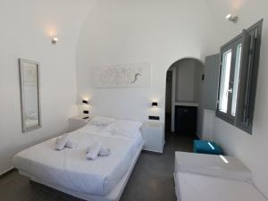 a white bedroom with two beds and a window at Perissa Economy Rooms in Santorini