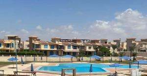 a swimming pool with blue umbrellas in front of houses at Coastal Comforts at Casabianca in Dawwār Muḩammad Abū Shanab