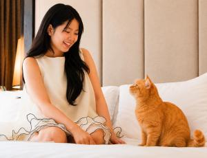 a woman sitting on a bed next to a cat at Mövenpick Hotel Sukhumvit 15 Bangkok in Bangkok