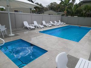 a swimming pool with white chairs next to a fence at Moby Dick Waterfront Resort Motel in Yamba
