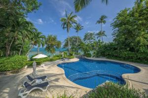 a swimming pool with chairs and trees and the ocean at Centara Villas Samui in Lamai