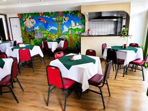 a restaurant with white tables and red chairs and a mural at Hotel Maragato in San José