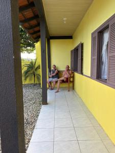 two men sitting on a bench on the porch of a house at Você vai sentir em casa in Itapoa