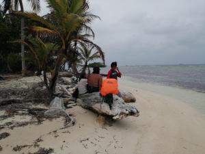a group of people sitting on a log on the beach at Isla Ganirdub in Río Azúcar