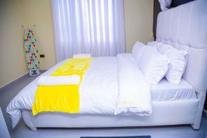 a white bed with a yellow blanket and white pillows at The VIP Afriqhomes in Nairobi