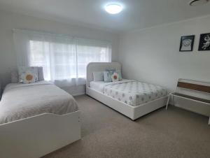 a white bedroom with two beds and a window at Alta House in Auckland