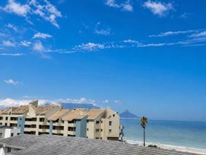 a building on the beach with a palm tree and the ocean at Modern Ocean View Apartment in Cape Town