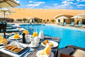 a table with breakfast food next to a swimming pool at Arabian Nights Resort & Spa in Shāhiq
