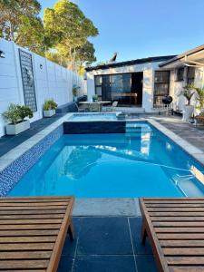 a swimming pool with two benches in front of a house at Bonita Vista Plattekloof in Cape Town