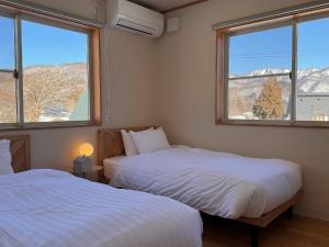 two beds in a room with two windows at Yamamori House in Hakuba