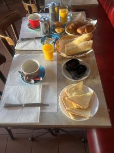 a table with plates of bread and cups of orange juice at Hôtel Au Bon coin chez Pierre in Franconville