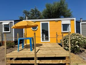 a yellow caravan with an umbrella and a wooden deck at Camping De Collignon in Cherbourg en Cotentin