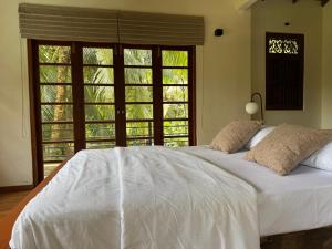 a bedroom with a large white bed with windows at Cinnamonhouse Villa in Poregedara