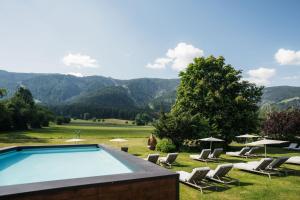 a swimming pool in a field with chairs and umbrellas at Hotel Montis - Active Nature Resort in Brunico