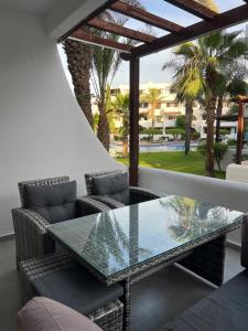 a glass table and chairs on a patio with palm trees at Appartement Cassia Vue Piscine rénovée cette année in Cabo Negro