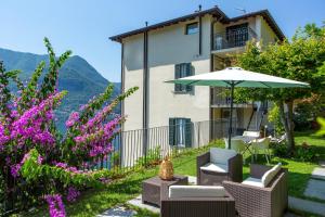 a patio with chairs and an umbrella and flowers at Emy House Charming Apt Stunning Views Balcony AC in Carate Urio