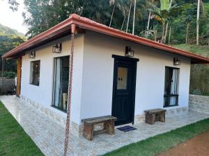 a small white house with a black door and benches at Lar temporário Rê Auer in Santa Teresa