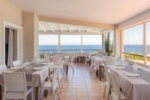 a restaurant with white tables and chairs and the ocean at Porto Skala Village Hotel in Skala +82 photos