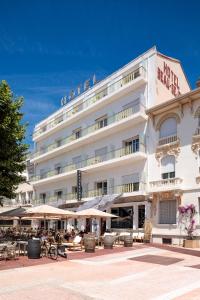 a large white building with tables and umbrellas at Le Beau Séjour in Saint-Raphaël