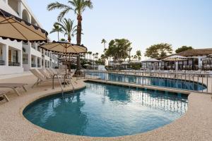 a pool at a resort with chairs and an umbrella at Wyndham Mallorca Portocolom Resort in Portocolom
