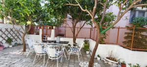 a patio with white chairs and a table and trees at Mama's Home in Chios