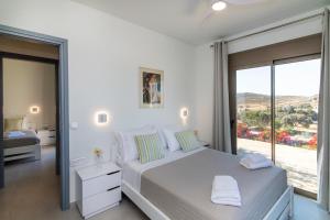 a white bedroom with a bed and a large window at Aegean Whispers in Agios Fokas