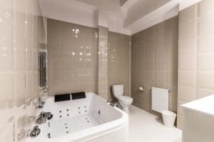 a white bathroom with a tub and a toilet at Gold and Silver Apartment - Manu SPA Lofts in Łódź