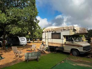 a rv parked in a field with chairs and a table at קרוואן עם חיוך in Odem
