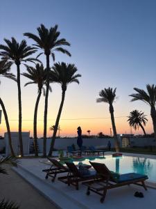 a pool with chairs and palm trees at sunset at Maison Rachid Djerba in El Guecheïne