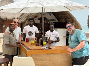 a group of men standing around a bar with an umbrella at Anchaca Sul in Bubaque