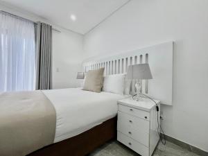 a white bedroom with a bed and a lamp on a nightstand at Number 12, Jadde apartments in Sandton