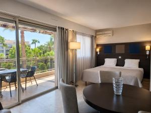 a hotel room with a bed and a table and a balcony at The Originals Résidence, Les Strélitzias in Juan-les-Pins