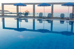 a swimming pool with chairs and umbrellas and the ocean at Porto Alegre Hotel in Kalamaki