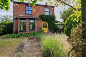 a brick house with a yellow door in a garden at Sandown, Spacious and Stylish in Southwold in Southwold